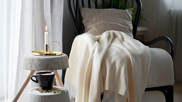 Sessel mit Decke neben Beistelltisch mit Kerze und Tasse