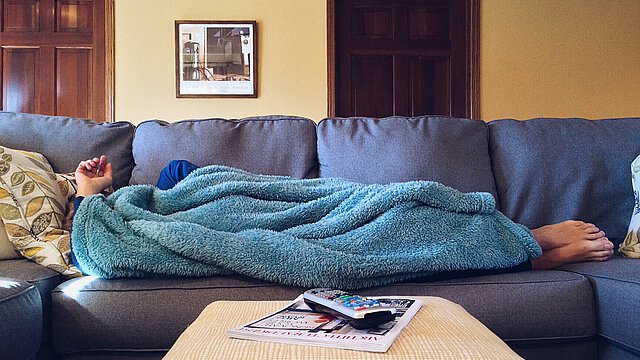 Person liegt mit Kuscheldecke auf Sofa