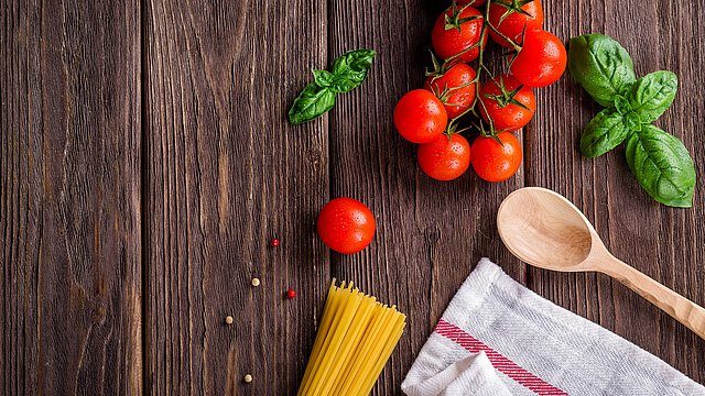 Holzbrett mit Kochlöffel und Pasta-Zutaten