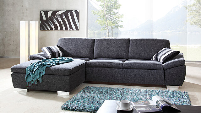 Graues Sofa mit Decke vor großer Fensterfläche